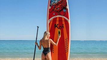 Una persona parada en la playa sosteniendo una tabla de remo con un diseño de dragón y la palabra "Koi".