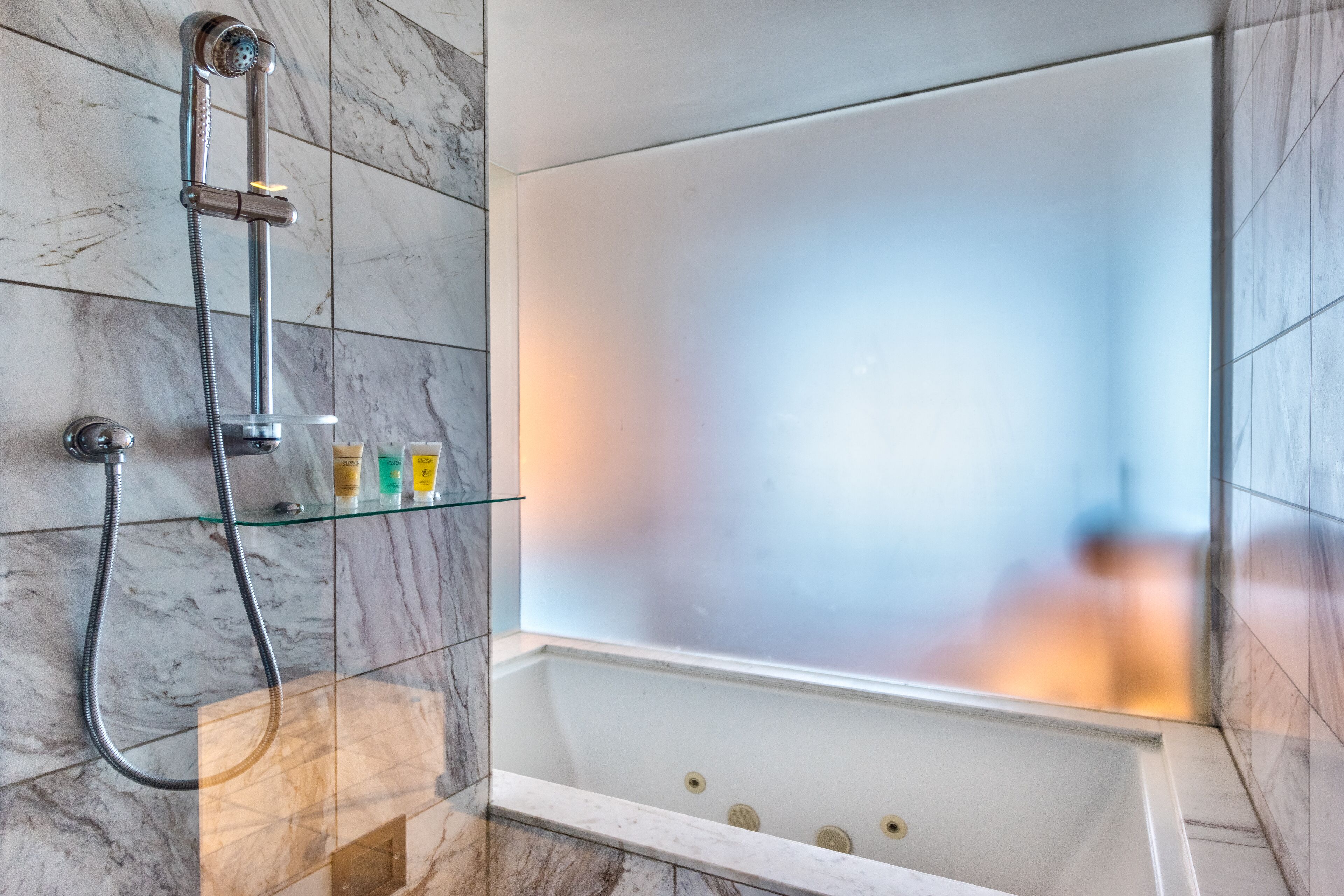 Een moderne badkamer met een douchecabine van glas, marmeren tegels en een bad.
