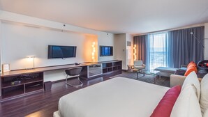 Une chambre d’hôtel moderne dotée d’un grand lit, d’un bureau avec un ordinateur, d’une télévision et d’un coin salon offrant une vue sur la ville.