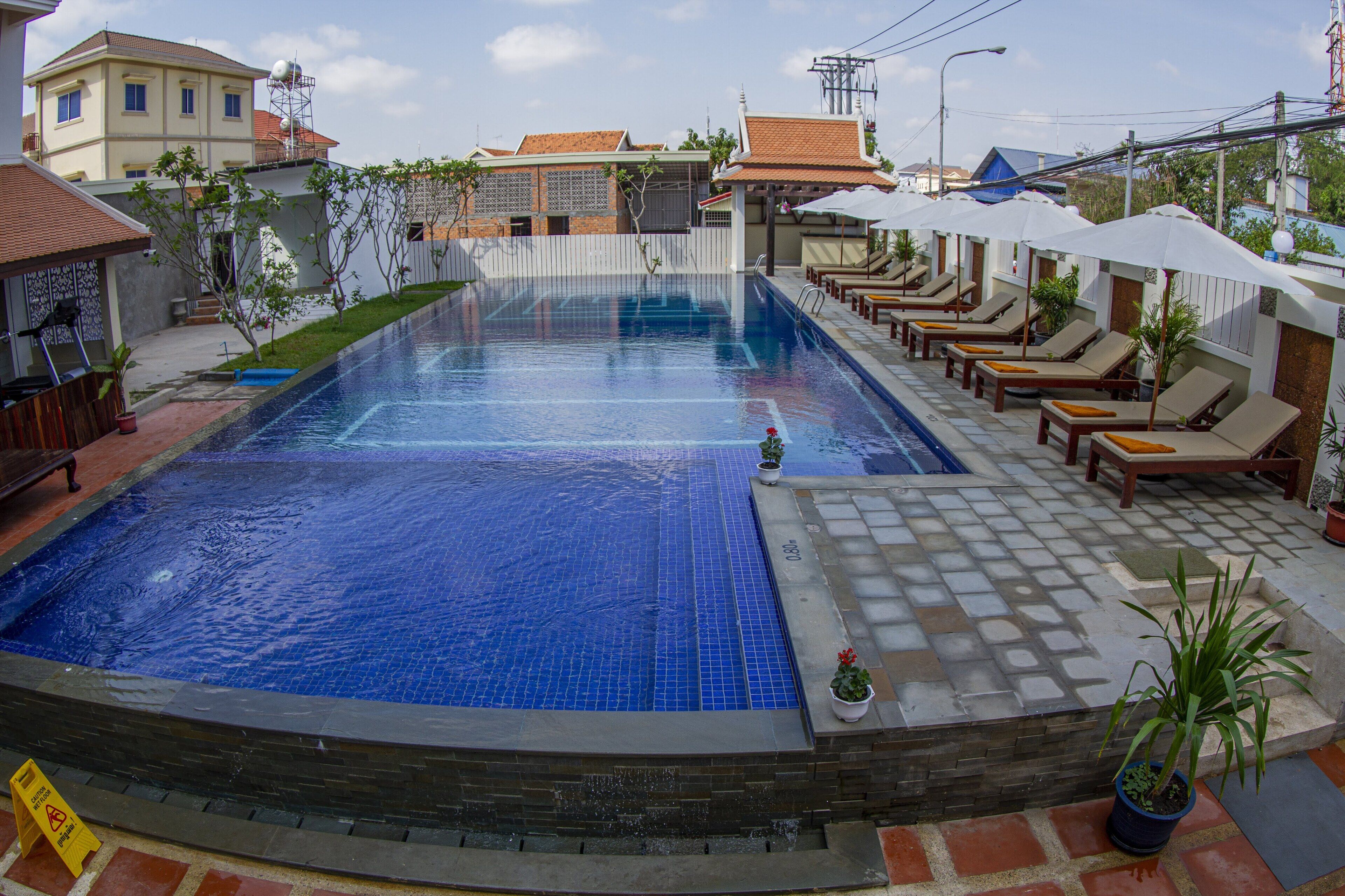 A swimming pool with lounge chairs and umbrellas, surrounded by a tiled deck and potted plants.