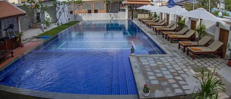 A swimming pool with lounge chairs and umbrellas, surrounded by a tiled deck and potted plants.