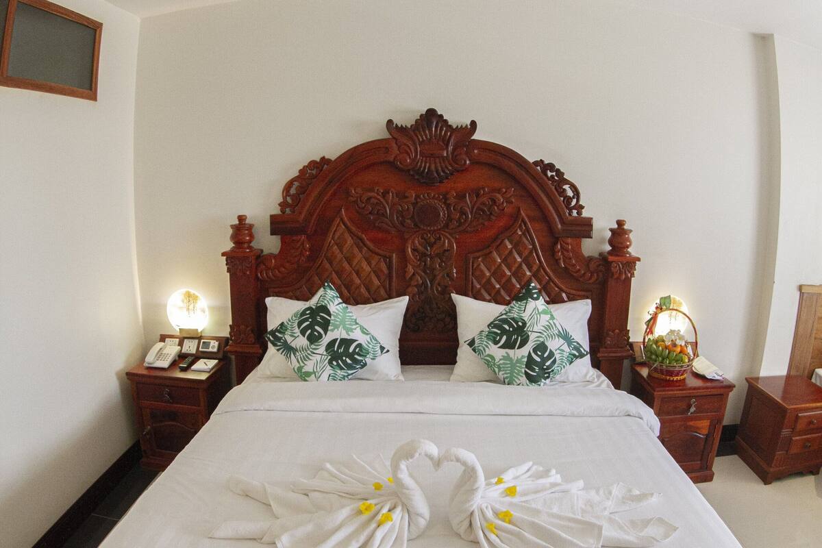 Una cama grande con cabecera de madera, dos mesitas de noche y una mesilla con lámpara.