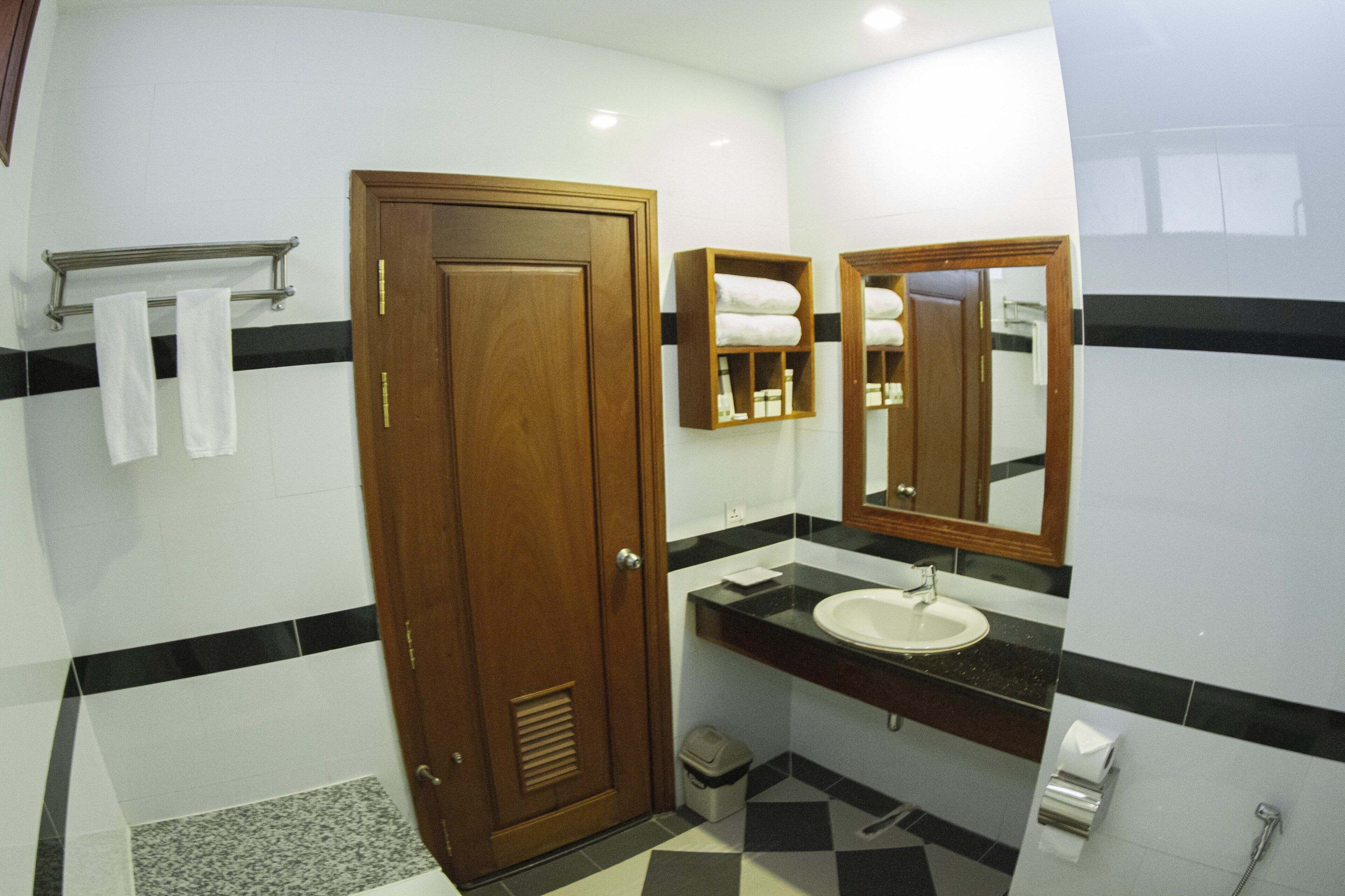 A bathroom with a wooden door, a sink, a mirror, and a towel rack.