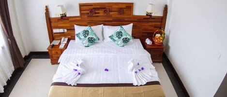 A neatly made bed with white and green floral pillows, a wooden headboard, and a bedside table with a lamp and a fruit basket.