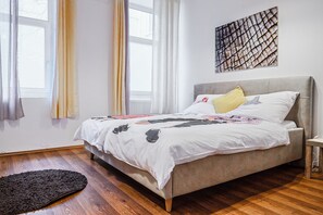 Ein Schlafzimmer mit Bett, einem fensterbelaubten Fenster, Holzboden und einem an der Wand befestigten Kunstwerk.