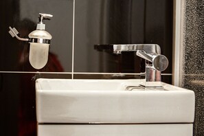 Ein Badezimmer mit einem weißen Waschbecken, einem Chrom-Wasserhahn und einer Seifenspender.