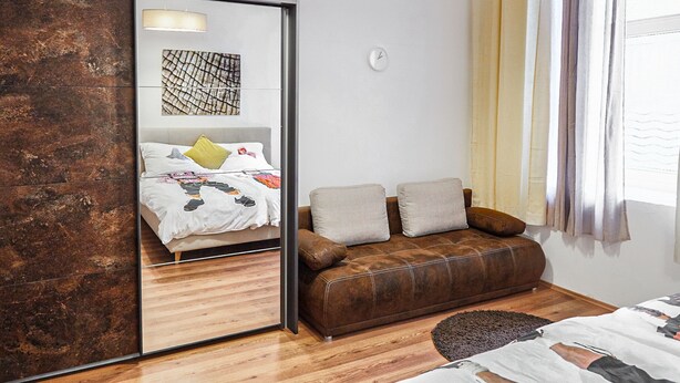 A modern bedroom with a large mirror, a brown leather sofa, a bed with a patterned bedspread, and a wall-mounted clock. - Modern Apartment in The Heart of Vienna 2 (Vienna)