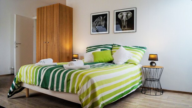 Quarto de hotel com uma cama, guarda-roupa de madeira, mesa de cabeceira com abajur e duas molduras na parede.