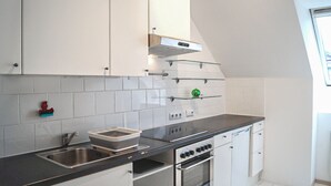 Uma cozinha com armários brancos, bancada preta, pia de aço inoxidável, forno embutido e um objeto decorativo verde em uma prateleira.