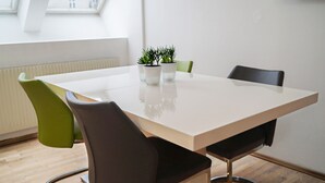 Uma sala de reunião moderna com uma mesa branca, cadeiras verdes e pretas, e plantas em vasos.