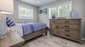 A bedroom with a bed, a wooden dresser, and a window with blinds. - Lakeside Serenity Villa with Private Patio (Bridgman)