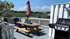 A wooden deck with a barbecue grill, picnic table, and umbrella.