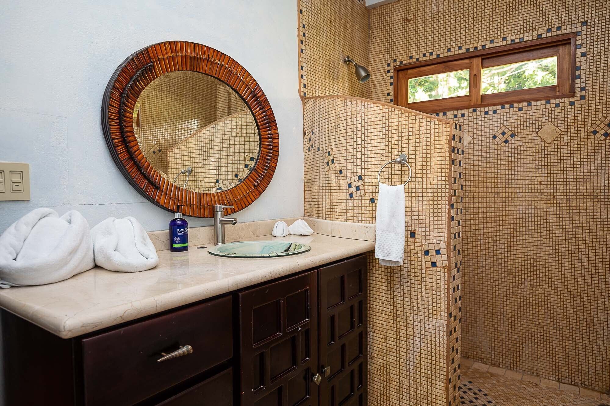 Ein Badezimmer mit rundem Spiegel, Waschbecken und Duschbereich mit Mosaikfliesen.