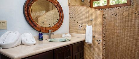 Ein Badezimmer mit rundem Spiegel, Waschbecken und Duschbereich mit Mosaikfliesen.