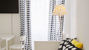 Una habitación con una mesa y sillas blancas, un radiador y cortinas de lunares.