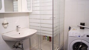 Un baño con lavamanos blanco, cabina de ducha de vidrio y lavadora de carga frontal.