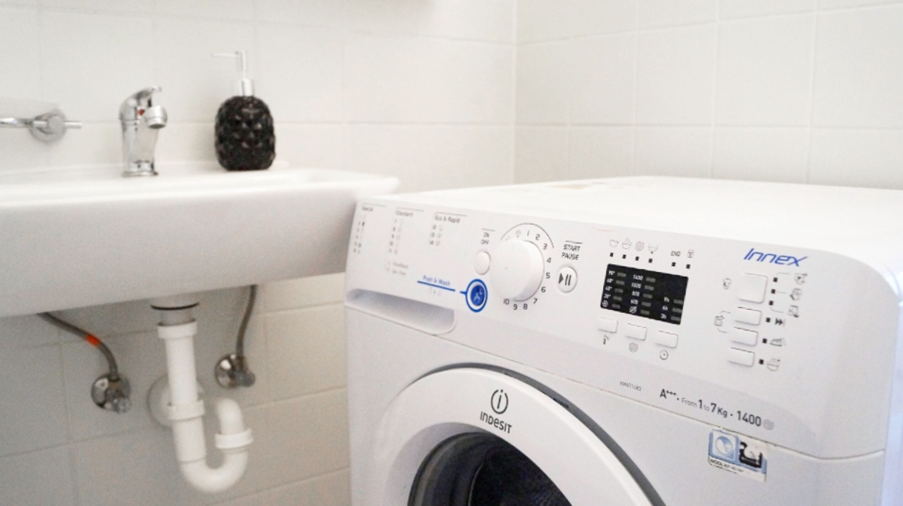 Una lavadora de carga frontal con panel de control digital, un lavabo con grifo y dispensador de jabón.
