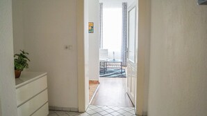 A narrow hallway with a potted plant on the left, leading to a room with a patterned rug, a chair, and a table. - Modern Apartment in The Heart of Vienna 5 (Vienna)