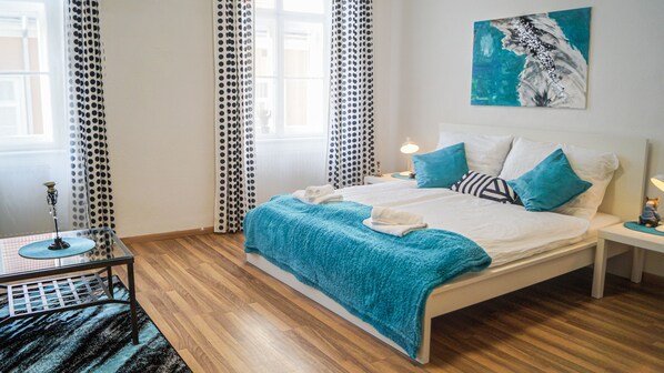 A neatly made bed with a blue blanket and pillows, a bedside table with a lamp, and a painting on the wall. - Modern Apartment in The Heart of Vienna 5 (Vienna)