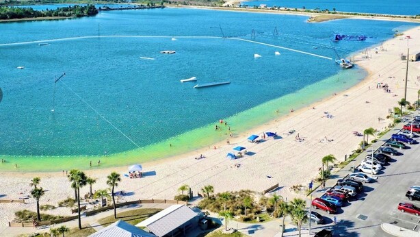 Ein Strand mit klarem, blauem Wasser, einem Parkplatz und einigen Gebäuden.