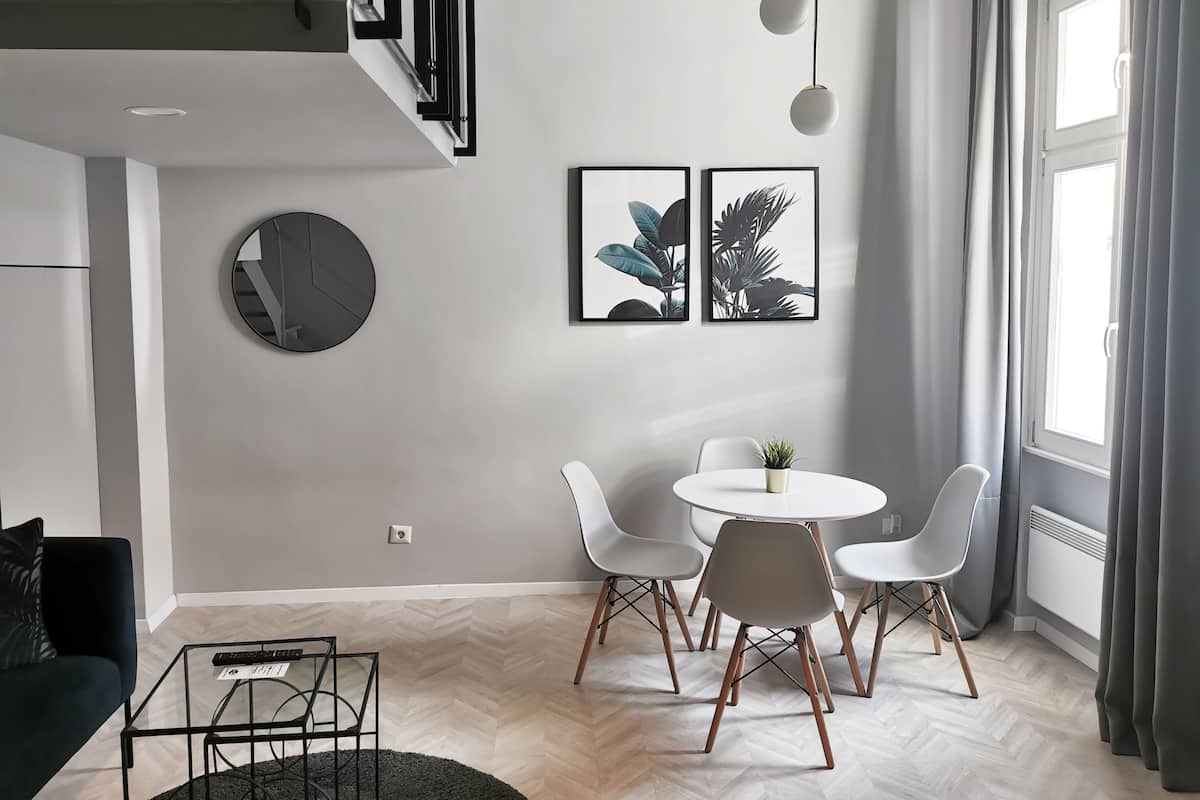 Un salon moderne avec une table basse ronde, des chaises blanches, une petite plante en pot et deux reproductions botaniques encadrées accrochées au mur.