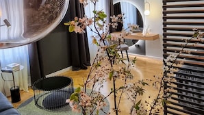 A modern living room with a curved mirror, a black metal chair, a wooden coffee table, and a potted plant with white flowers. - Mint Boutique Studio Apartments  (Zagreb)