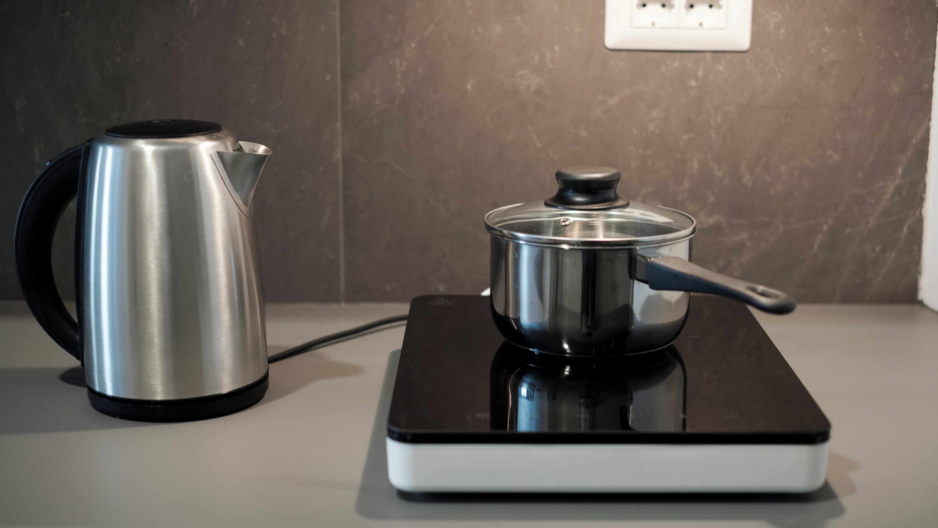 A kettle and a pot on a black induction cooktop.