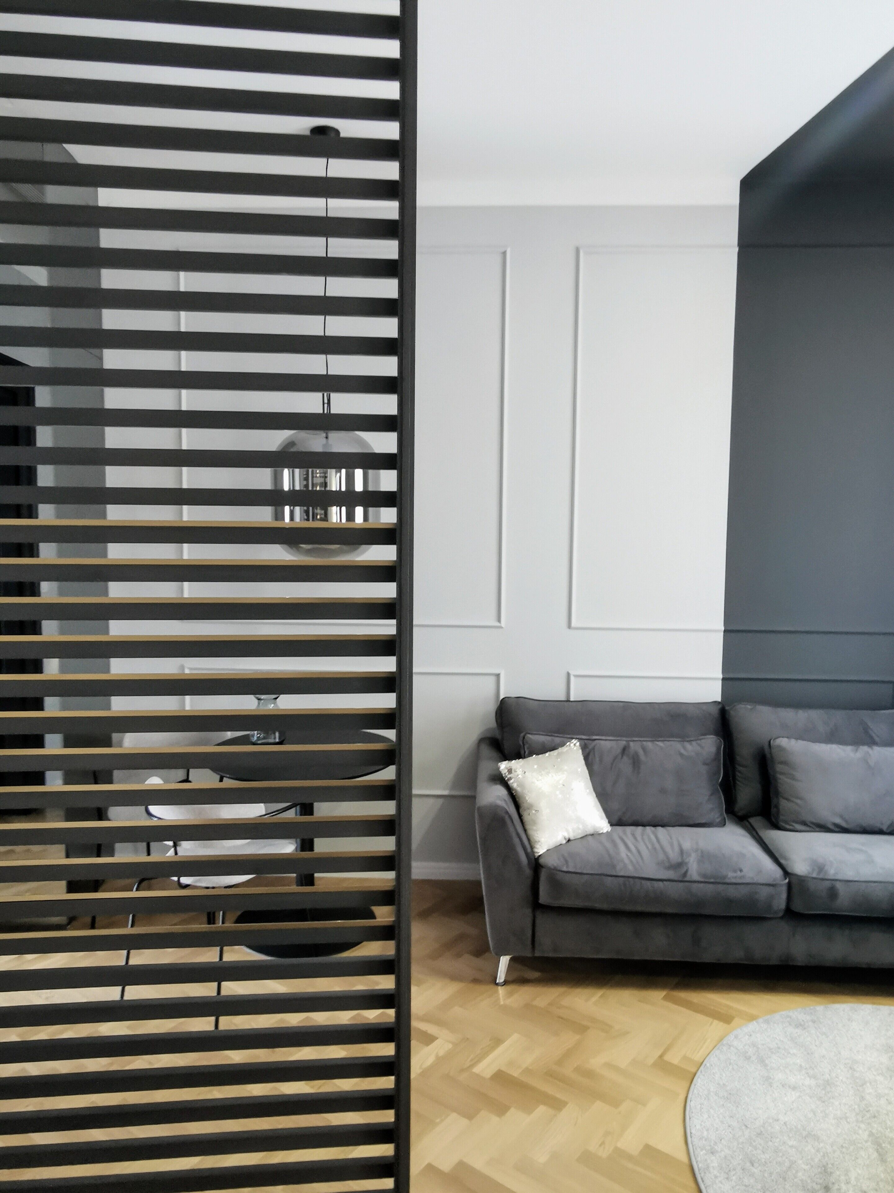 A modern living room with a grey sofa, a round rug, and a wooden floor.