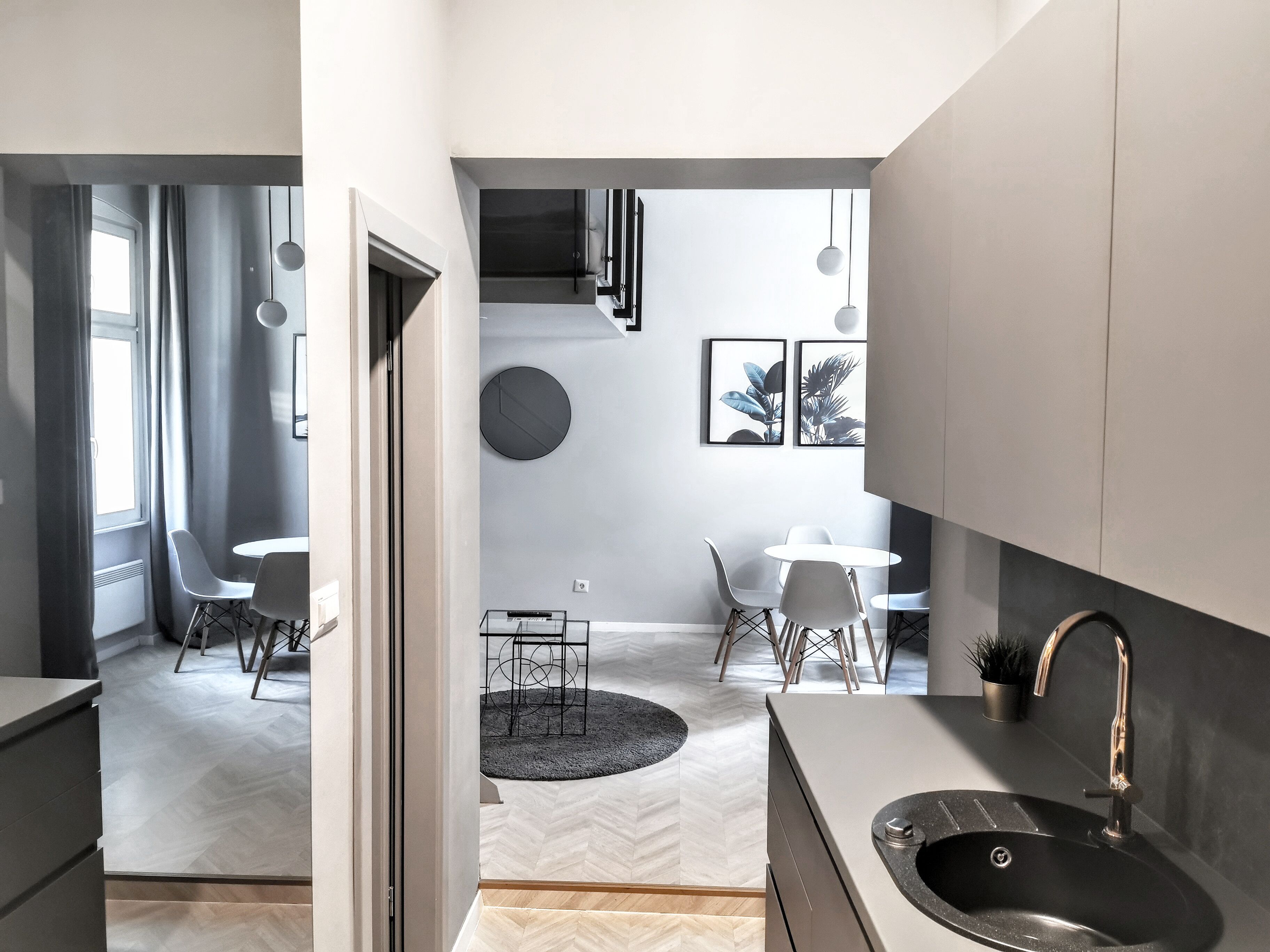 Eine moderne Küche mit einer großen Spüle, ein Essbereich mit zwei Tischen und Stühlen sowie Blick in einen Wohnraum mit einer Treppe.