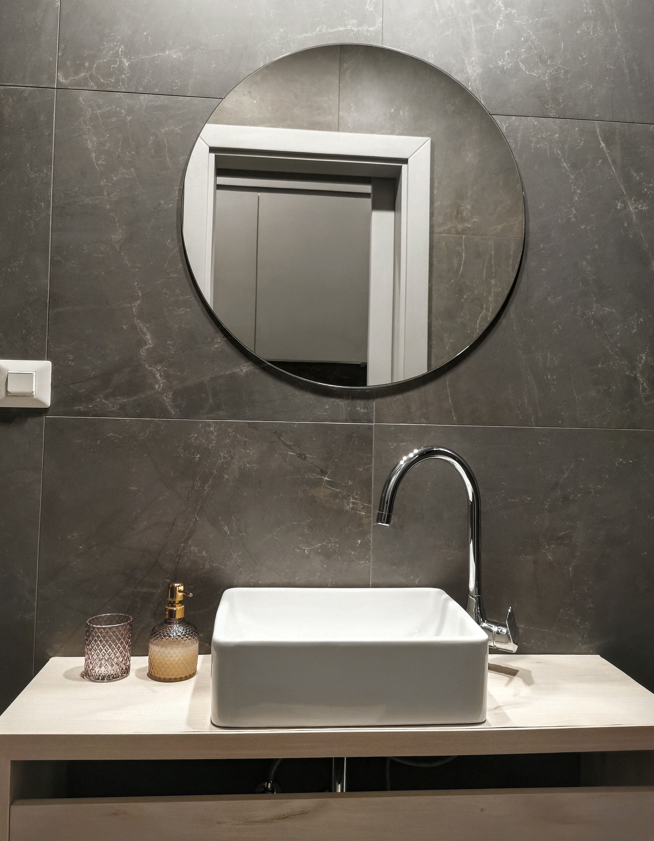 Un baño con un lavamanos rectangular, un espejo redondo y un grifo.
