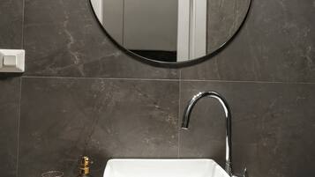 Un baño con un lavamanos rectangular, un espejo redondo y un grifo.