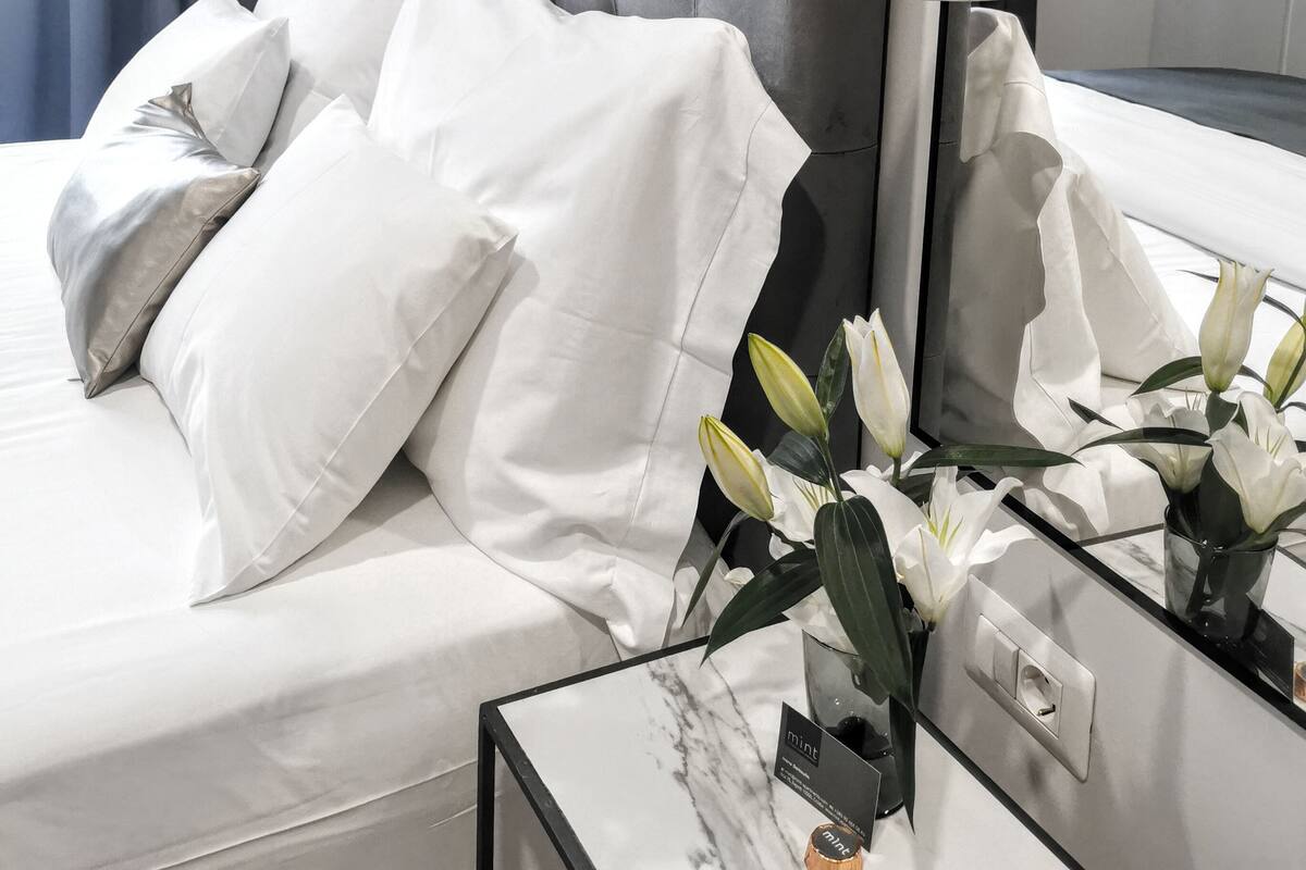Une chambre d’hôtel moderne avec une tête de lit capitonnée, du linge de lit blanc et une table de chevet en marbre agrémentée d’un vase de fleurs.