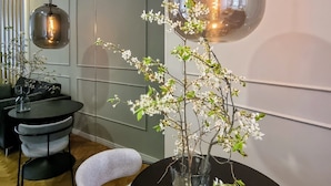 A modern dining area with a round table, a vase with white flowers, and a hanging light fixture. - Mint Boutique Studio Apartments  (Zagreb)