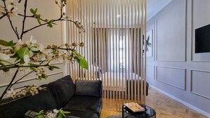 A modern living room with a black leather sofa, a round coffee table, and a wooden partition with vertical slats. - Mint Boutique Studio Apartments  (Zagreb)