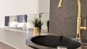 Et moderne badeværelse med en sort vask, guldfarvet armatur og en lille plantepotte.