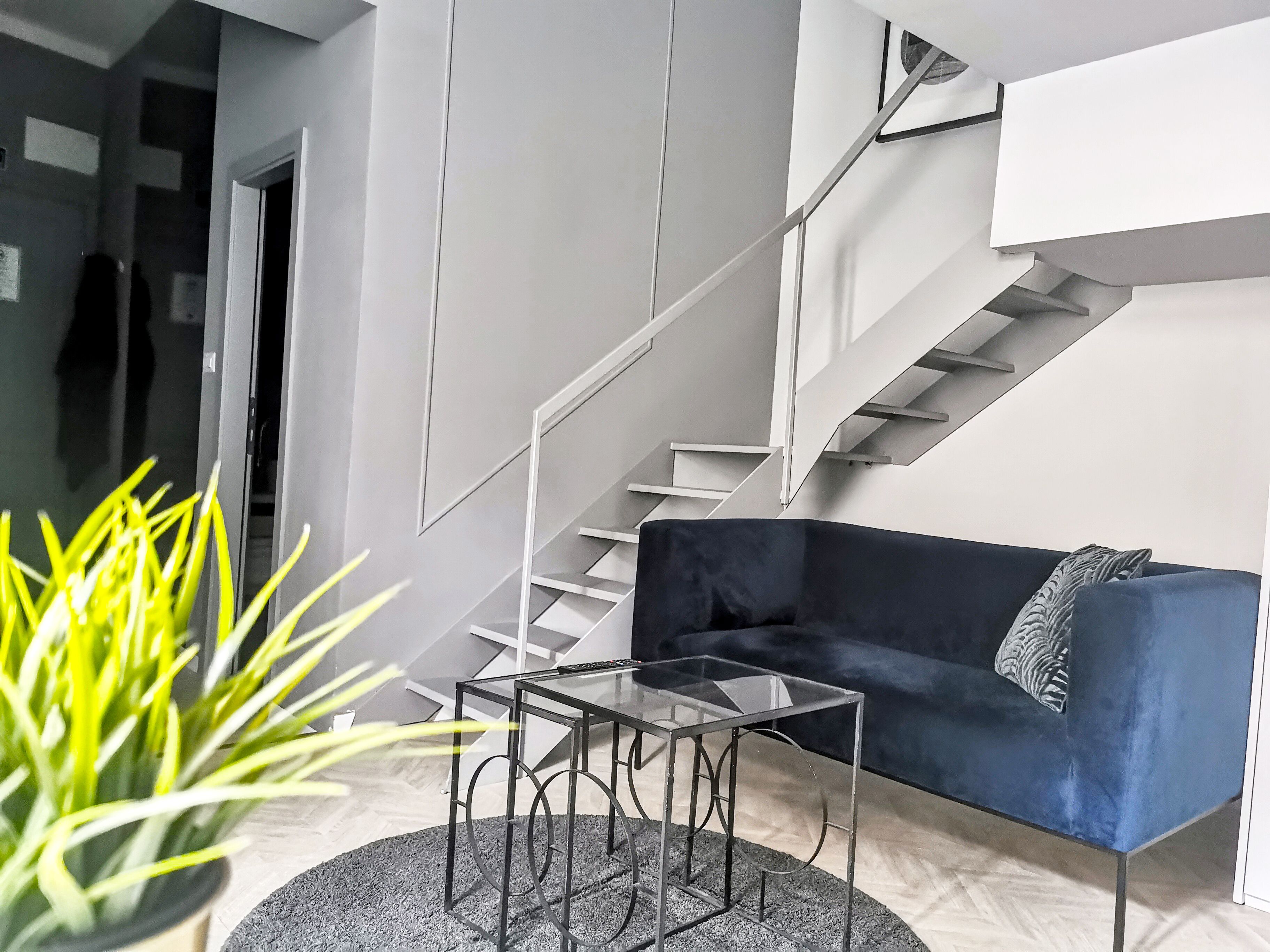 A modern living room with a dark blue sofa, a glass coffee table, and a staircase with white railings.