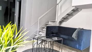 A modern living room with a dark blue sofa, a glass coffee table, and a staircase with white railings.