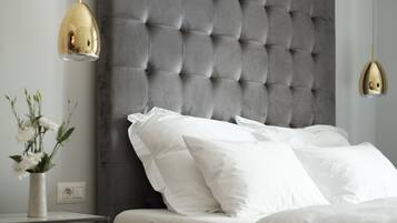 A bedroom with a tufted headboard, white bedding, and a vase of flowers on a bedside table.