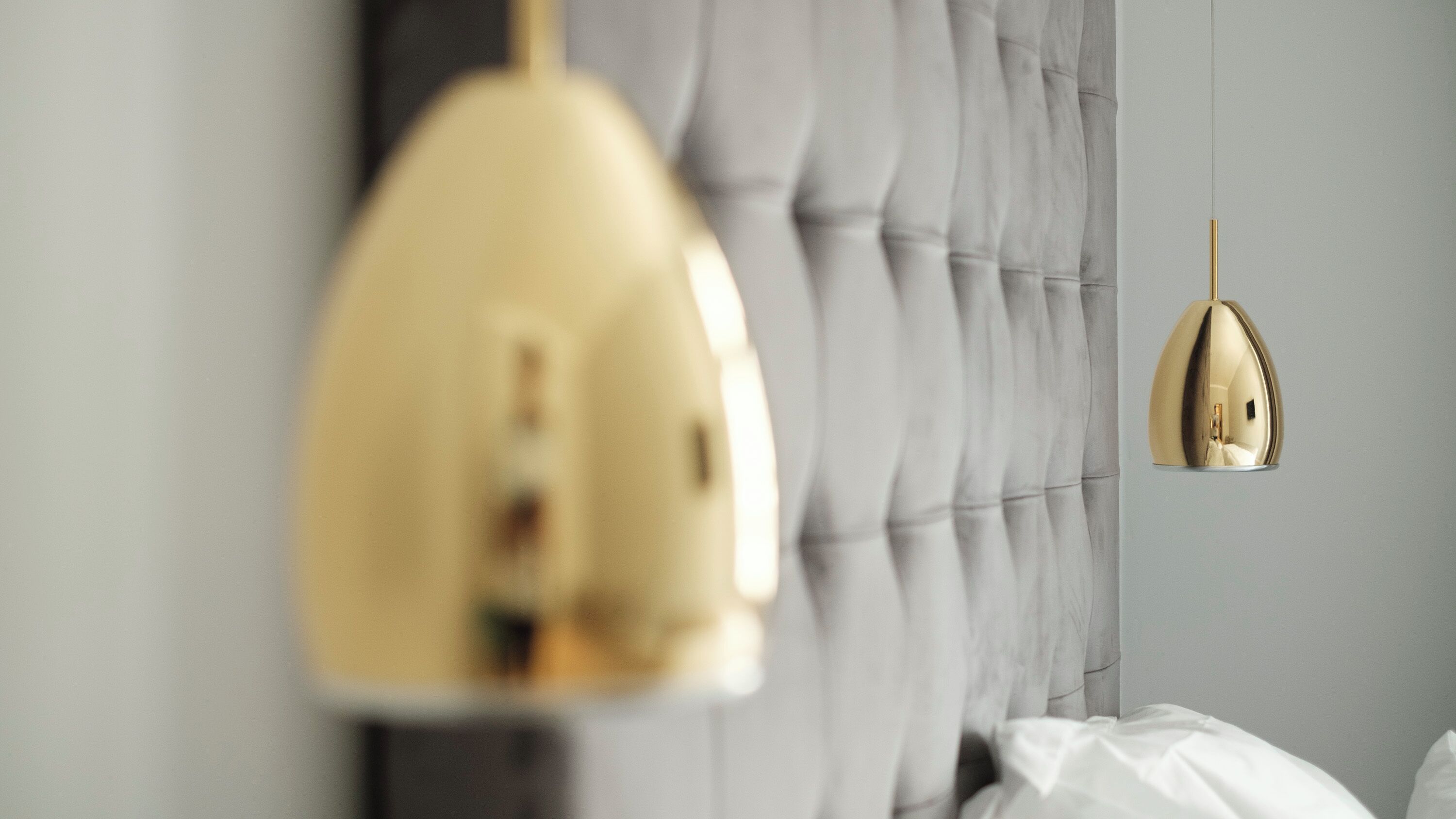 A bedroom with a tufted headboard, a gold pendant lamp, and a wall-mounted light fixture.