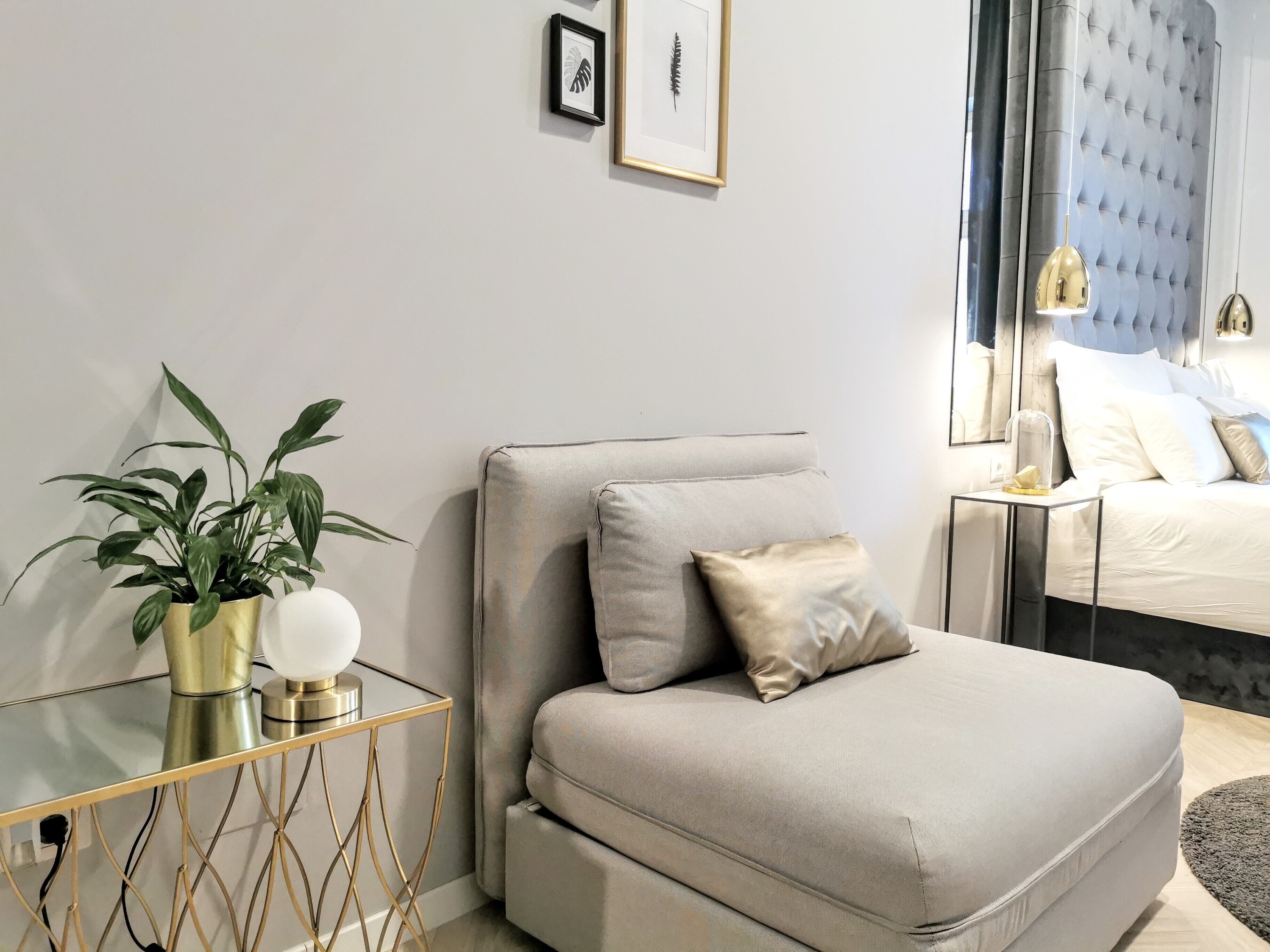 Un dormitorio moderno con sofá cama, mesita de noche con lámpara, planta en maceta y cuadros en la pared.