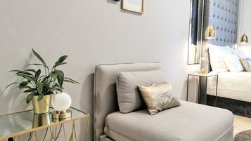 Un dormitorio moderno con sofá cama, mesita de noche con lámpara, planta en maceta y cuadros en la pared.