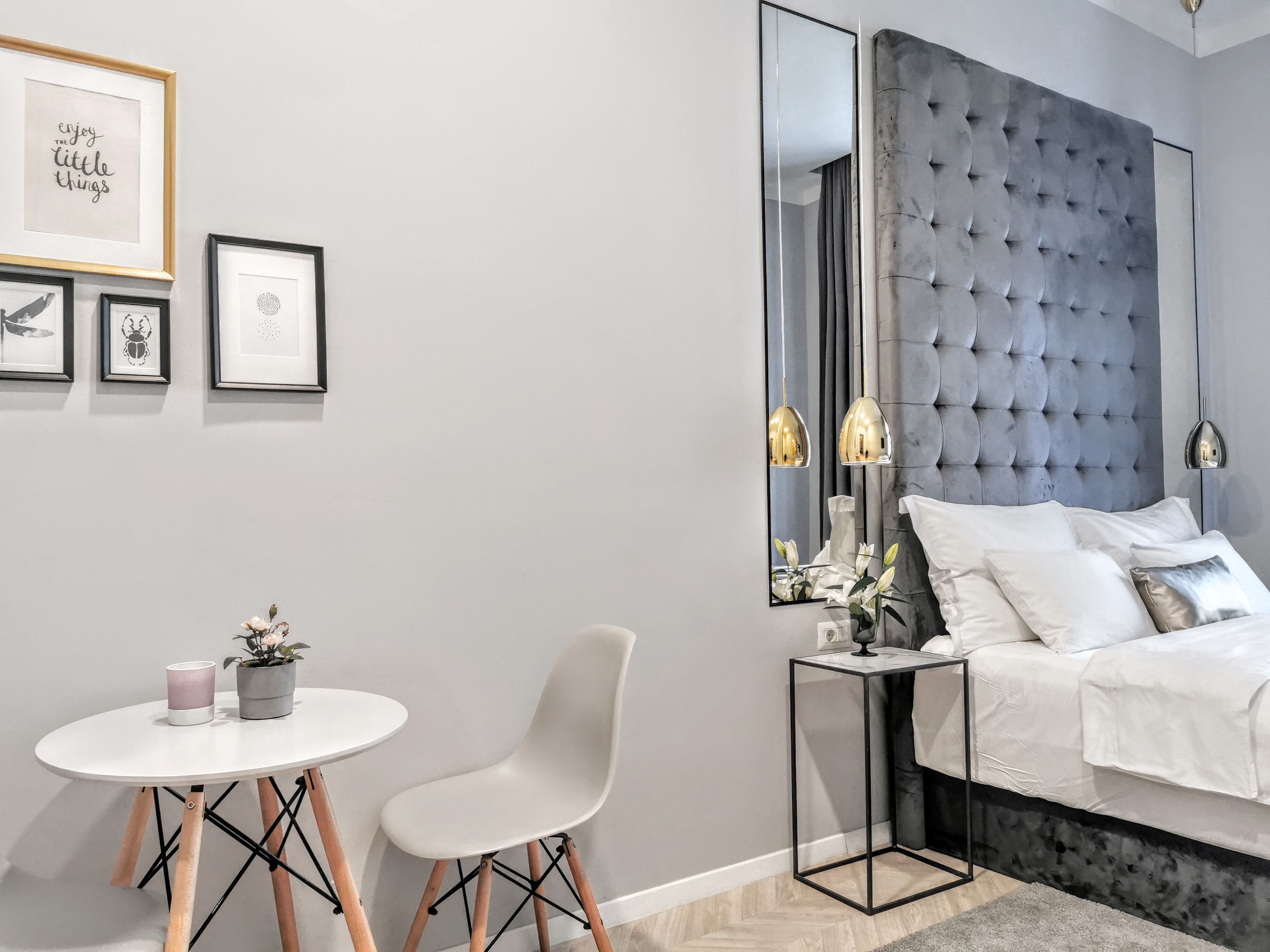 Camera da letto moderna con testiera imbottita, un grande specchio, un comodino, un letto bianco e un piccolo tavolo rotondo con sedie.