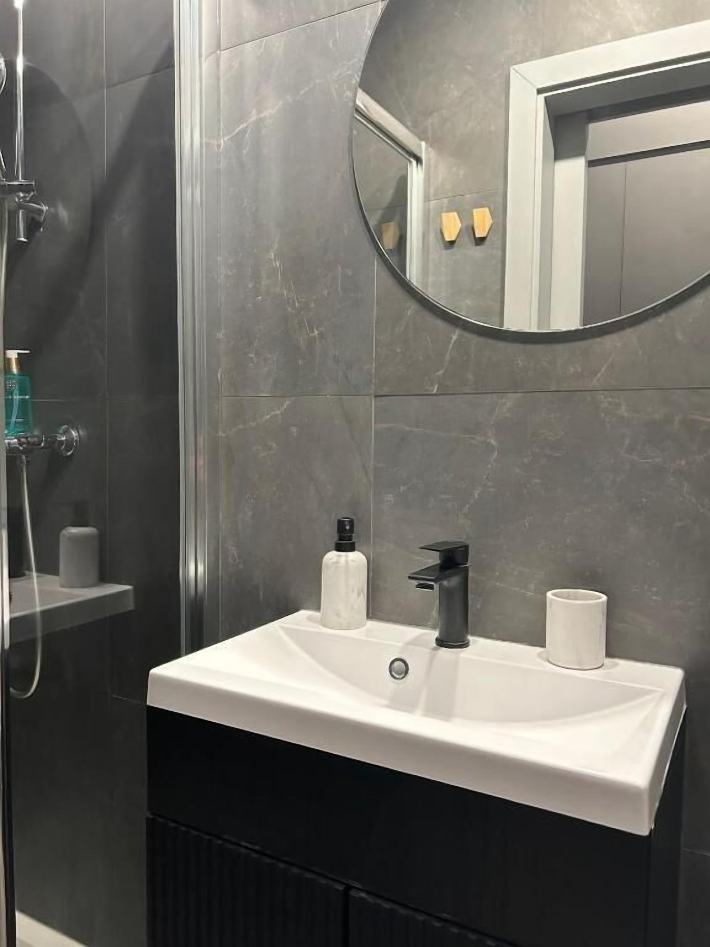 A modern bathroom with a white sink, black faucet, and a round mirror above it.