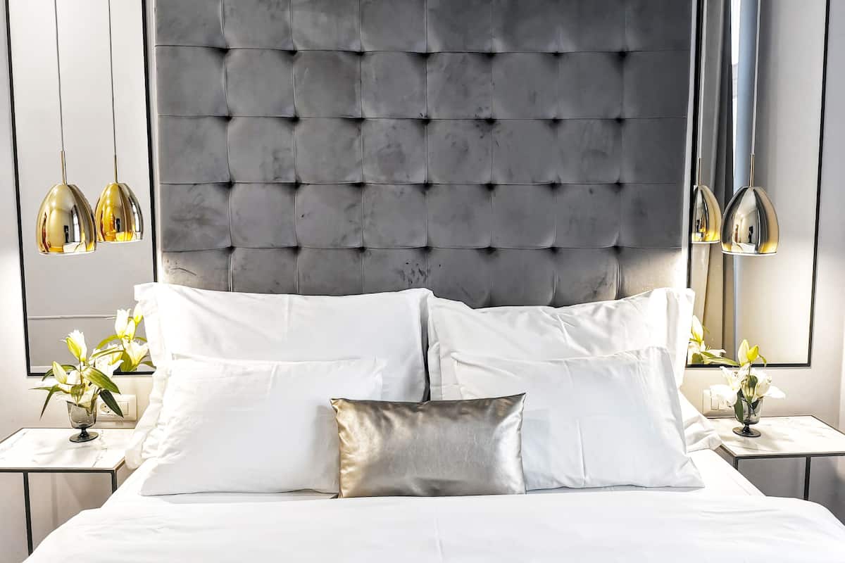 Une chambre à coucher avec une tête de lit capitonnée, du linge de lit blanc et deux tables de chevet ornées de lampes et de fleurs.