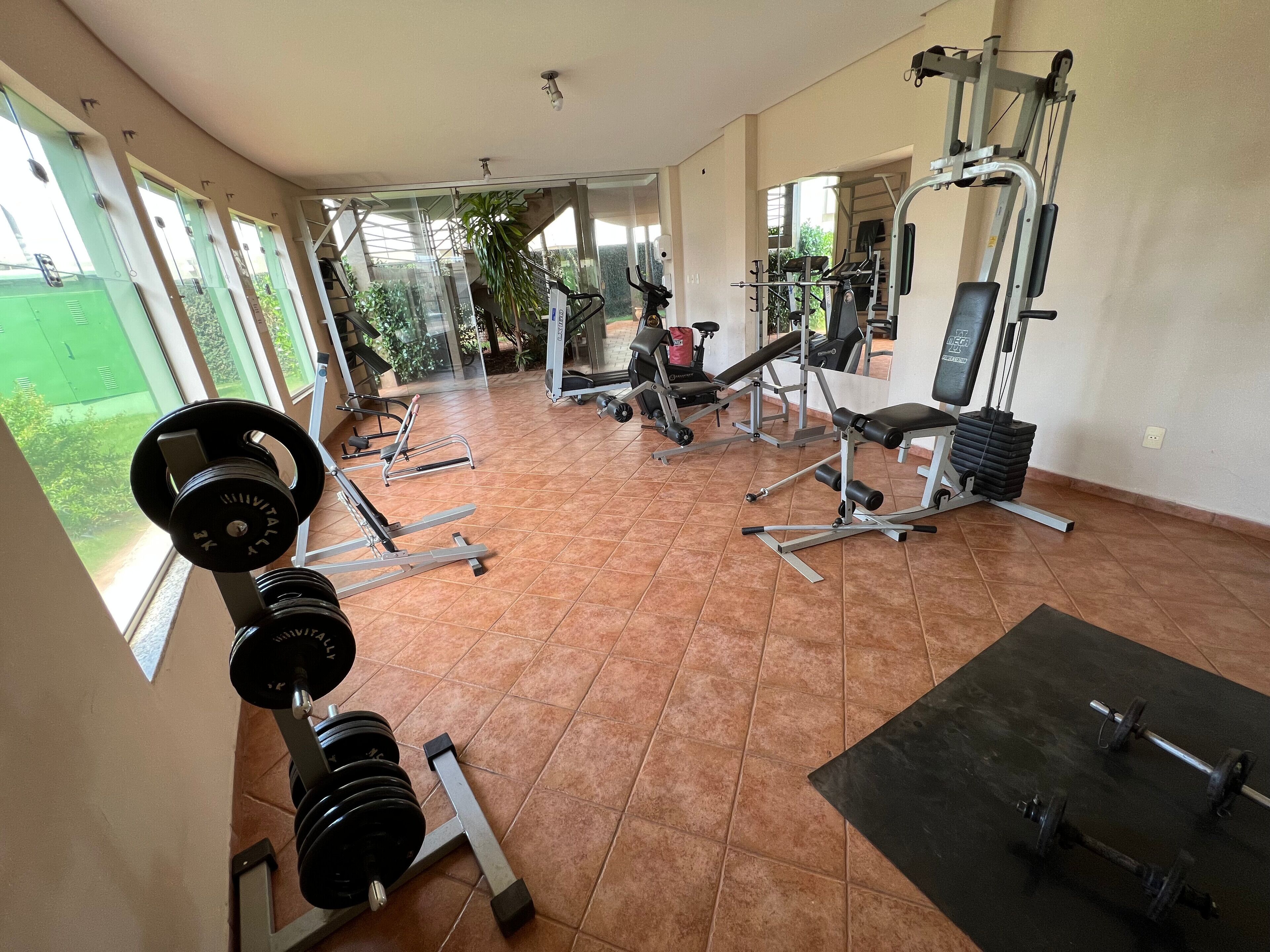 Une salle de sport équipée de divers appareils d’exercice, dotée de grandes fenêtres et offrant une vue sur la verdure environnante.