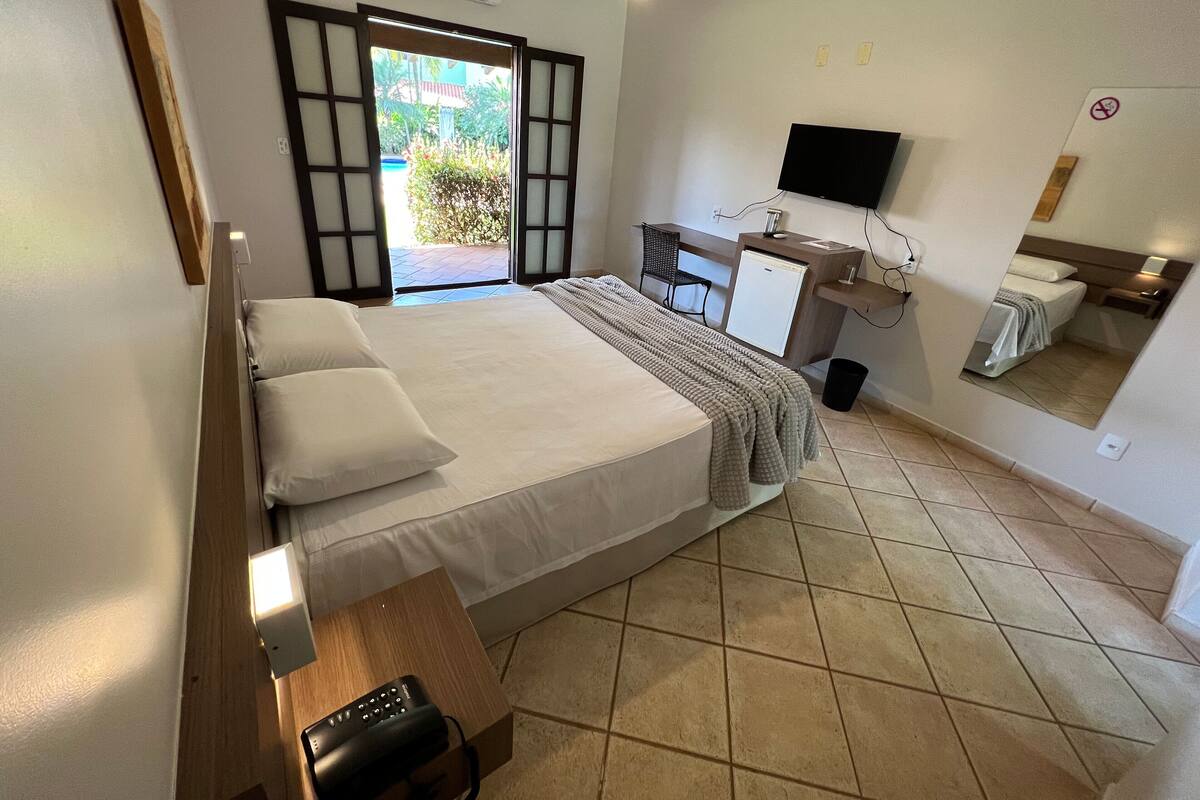 A hotel room with a bed, a desk, a chair, a TV, and a mirror.