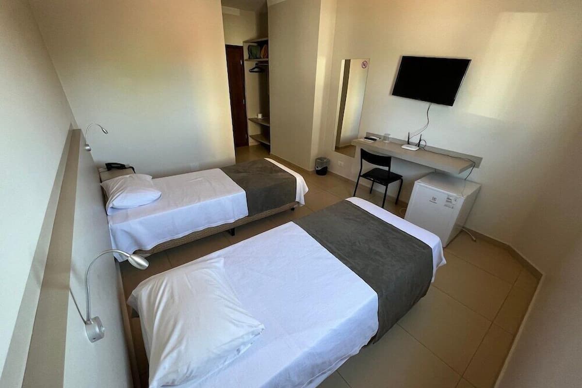 A hotel room with two beds, a desk, a chair, a TV, and a mirror.