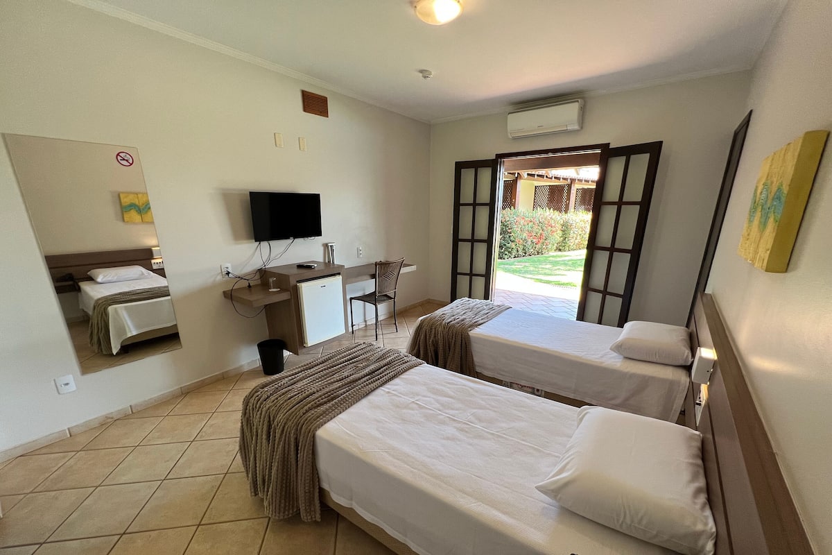 A hotel room with two beds, a desk, a chair, a TV, and an air conditioning unit.