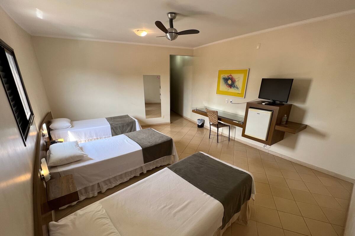 A hotel room with two beds, a desk with a chair, a television, and a ceiling fan.