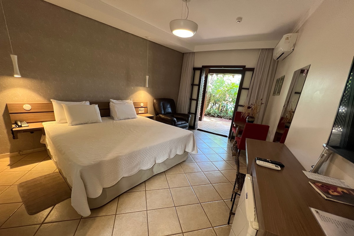 A hotel room with a large bed, a desk with a chair, a telephone, and a window with curtains.